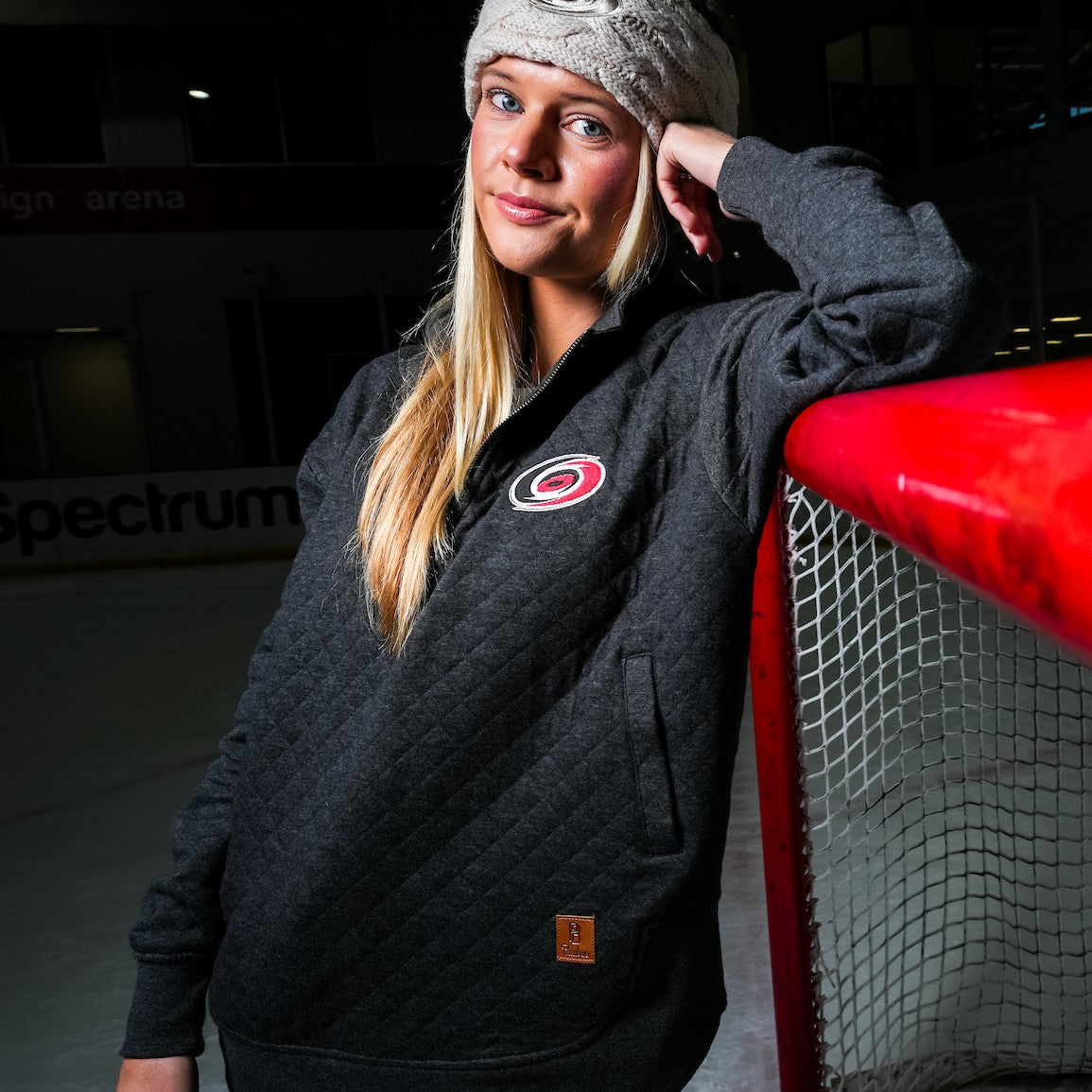 The jacket being worn by a model standing on an ice rink, leaning on a net