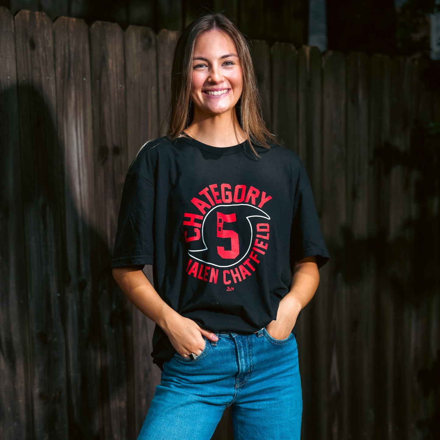 The t-shirt being worn by a model outside in front of a fence