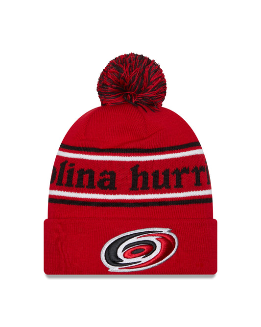 Front View: Red cuffed beanie with pom that says Carolina Hurricanes with Hurricanes primary logo on cuff