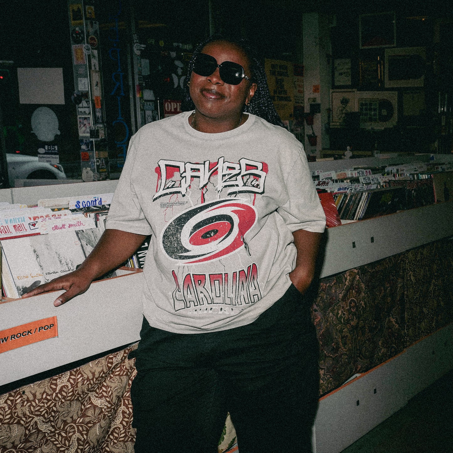 Model posing wearing the tee in a record store