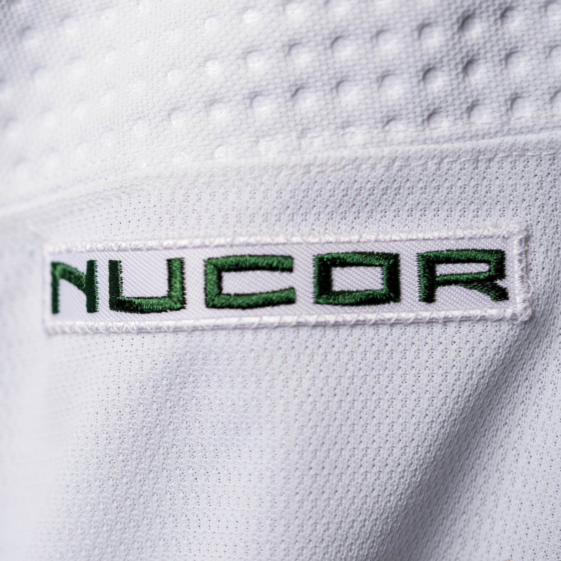 White patch with NUCOR logo in green lettering