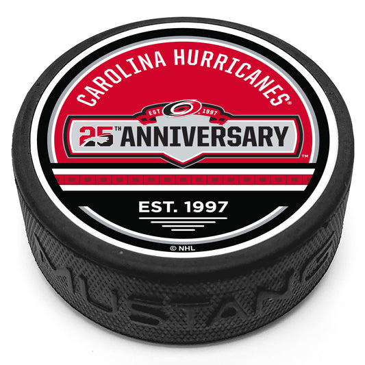 Hockey puck with the Hurricanes 25th Anniversary jersey patch logo in the center with "Carolina Hurricanes" above and our signature flag stripe with the phrase "Est. 1997" below on a red and black top face.