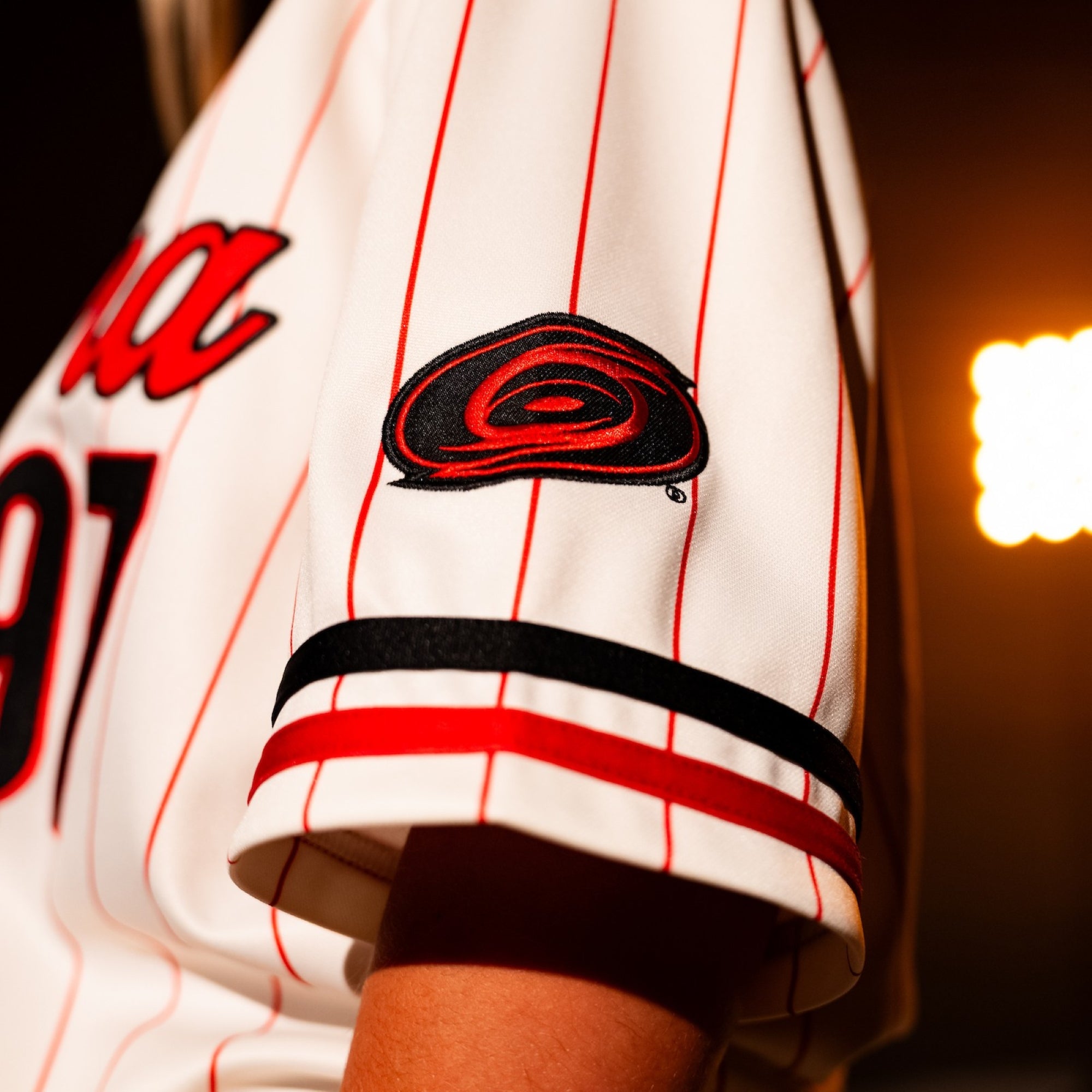 Close up of left sleeve: Tonal logo with black/red stripe below, red pinstripes