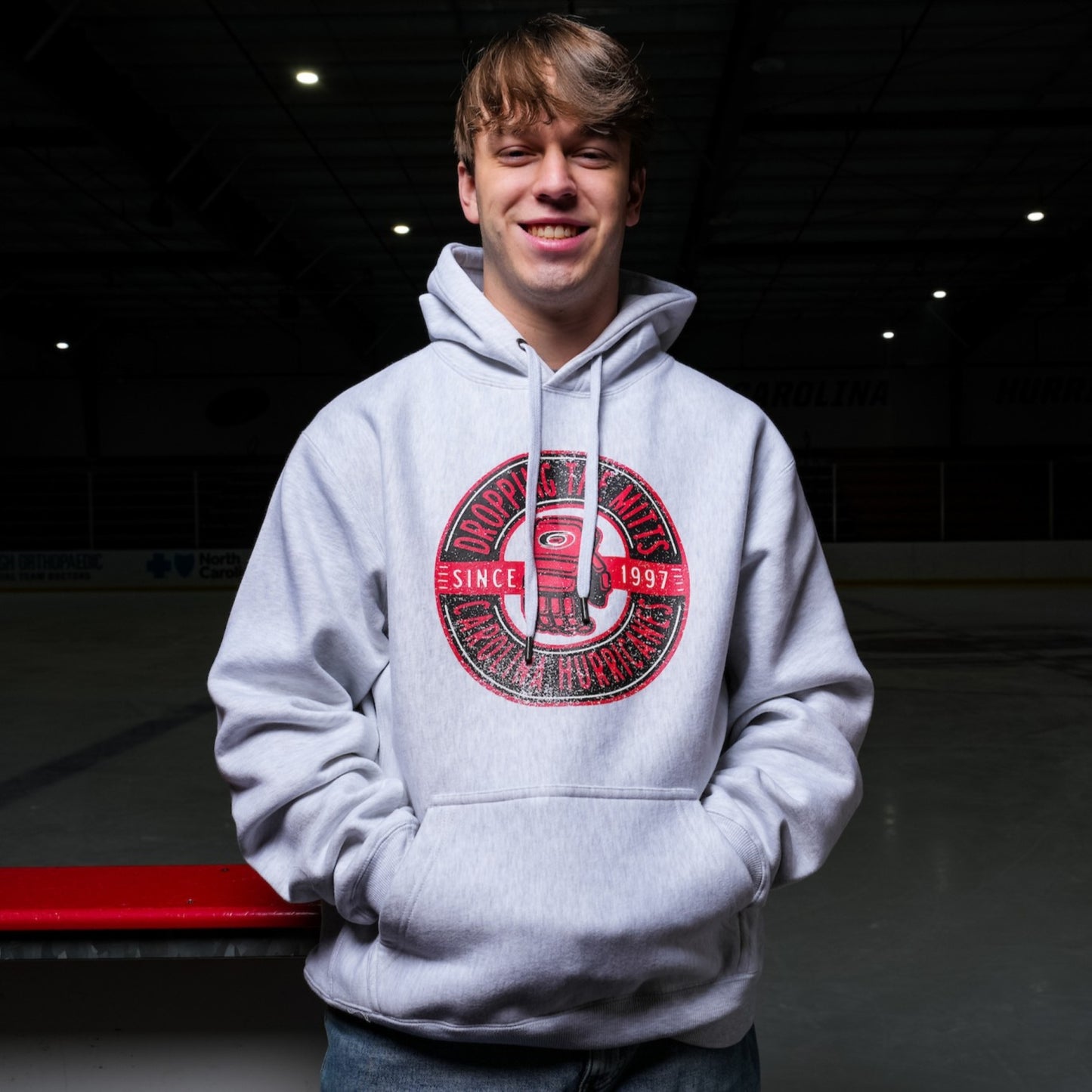 The hoodie being worn by a model while standing on a hockey bench