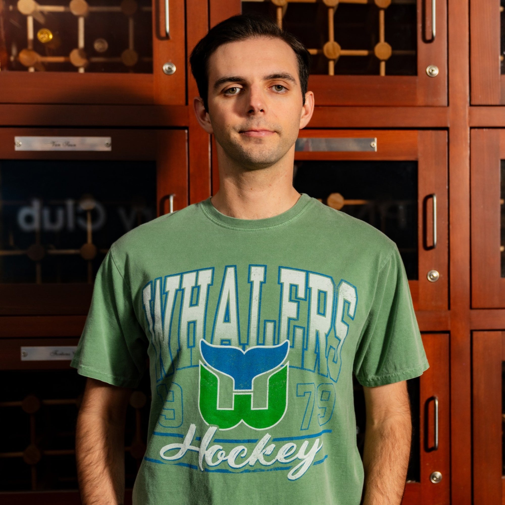 The tee being worn by a Caniac in front of a wooden cabinet