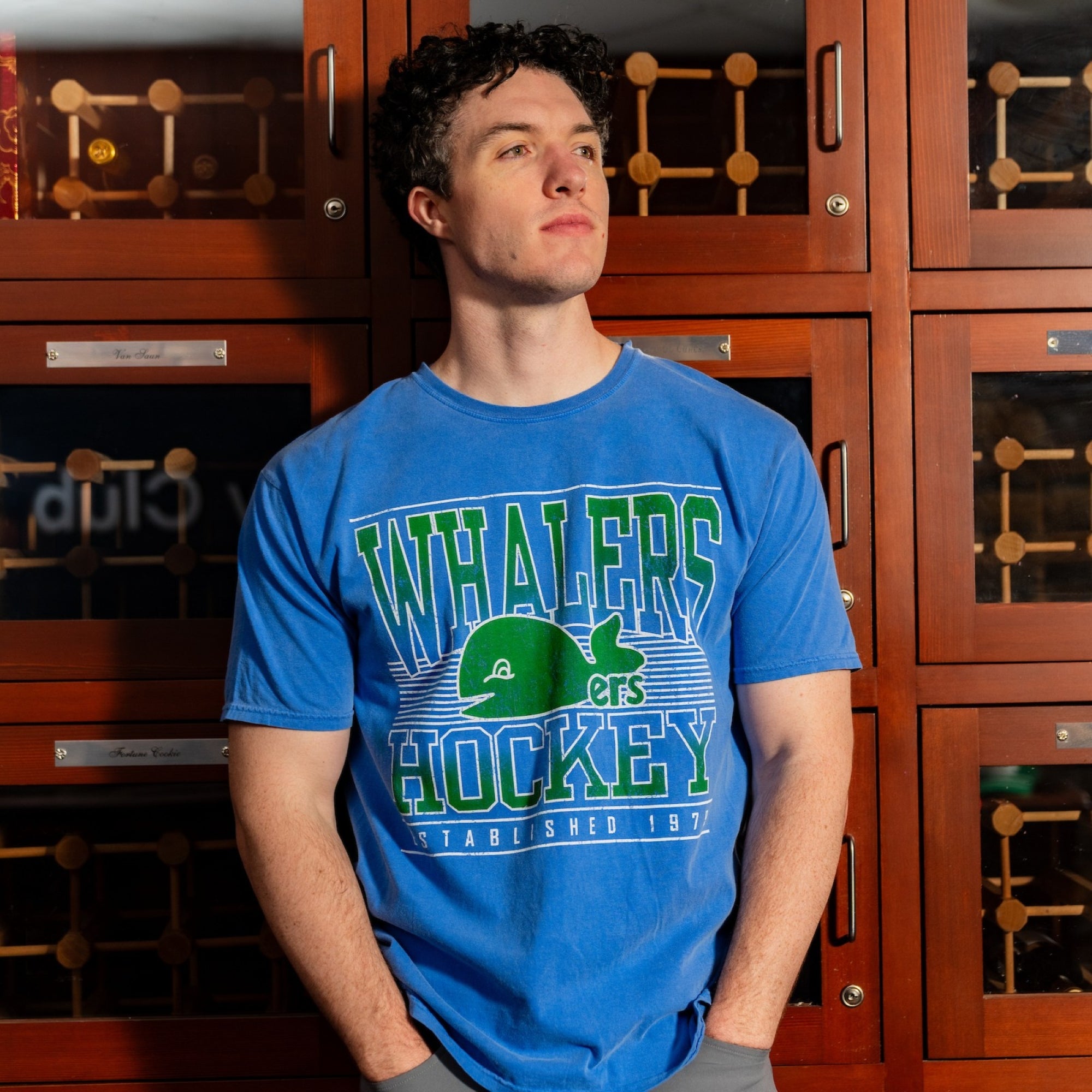 The tee being worn by a Caniac in front of a wooden cabinet