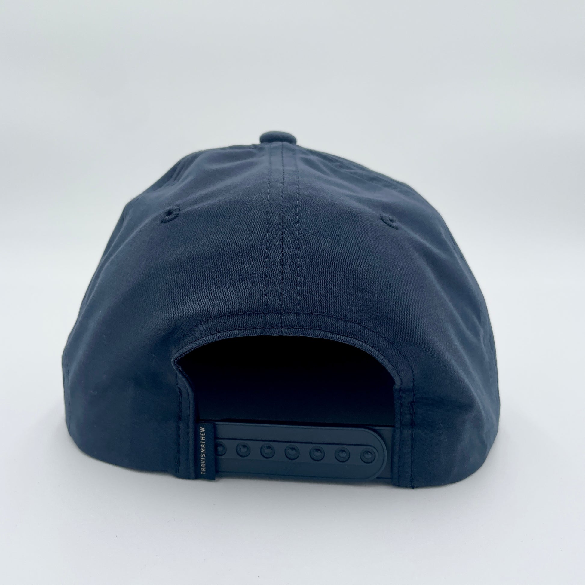 Back: Navy blue hat with navy snapback straps, Travis Mathew tag on straps