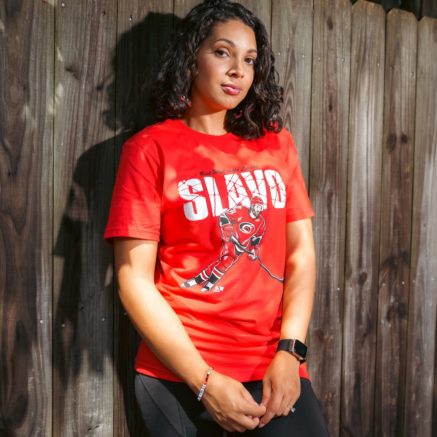 The t-shirt being worn by a model outside in front of a fence
