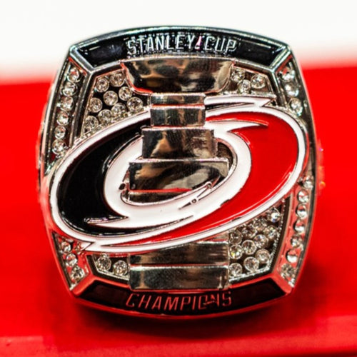 Front: Primary logo with Stanley Cup through middle of logo in front of studs, "STANLEY CUP CHAMPIONS"