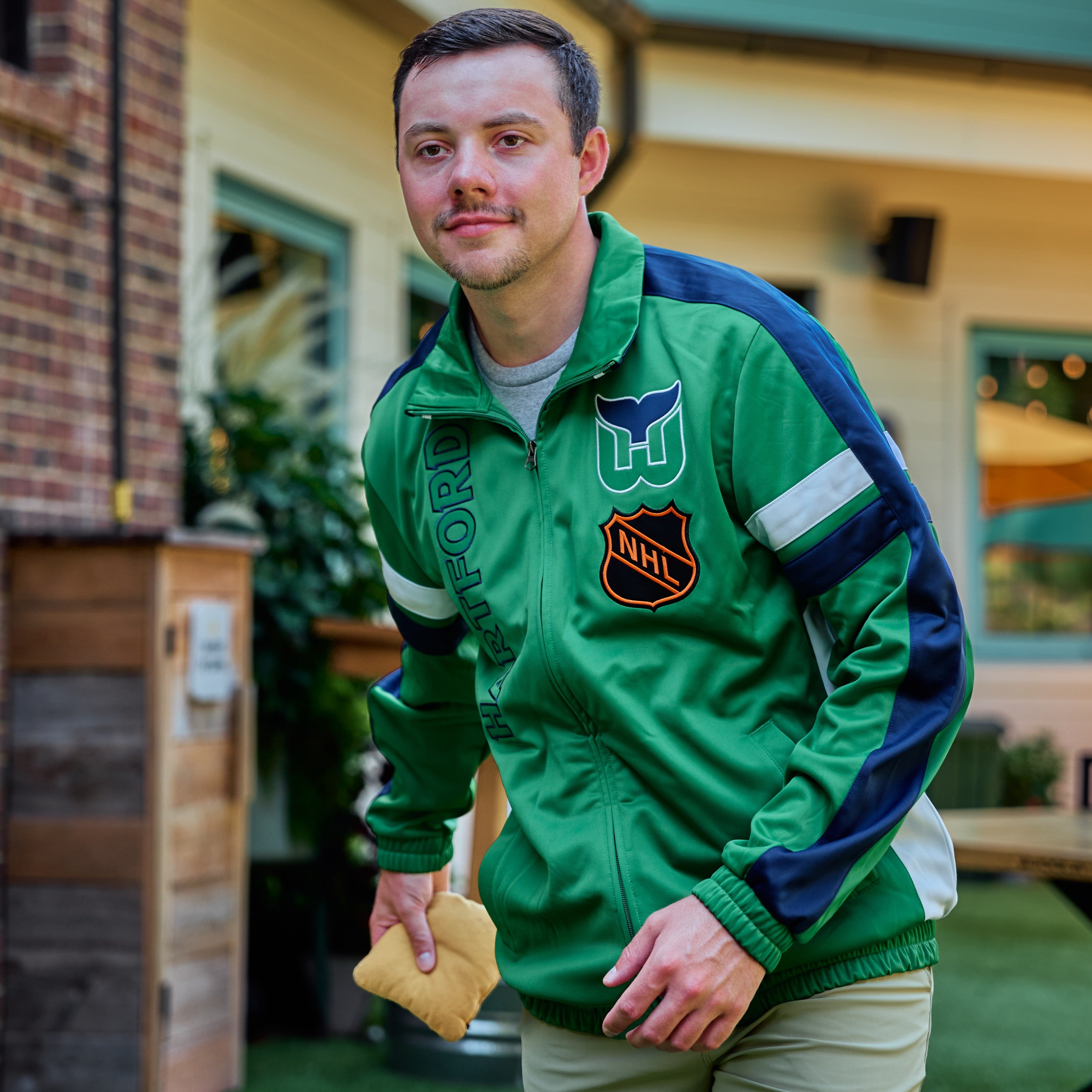 The jacket being worn by a model that is playing cornhole