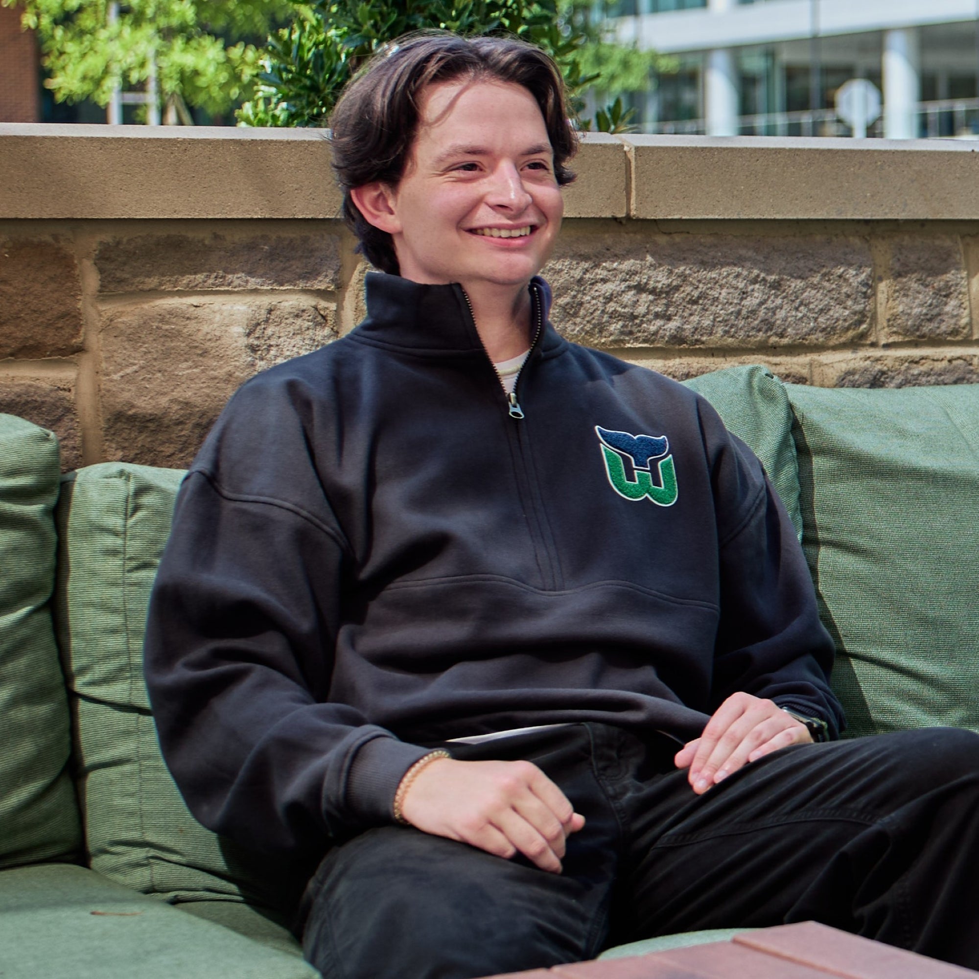 The quarter-zip being worn by a model outdoors while they sit on a couch
