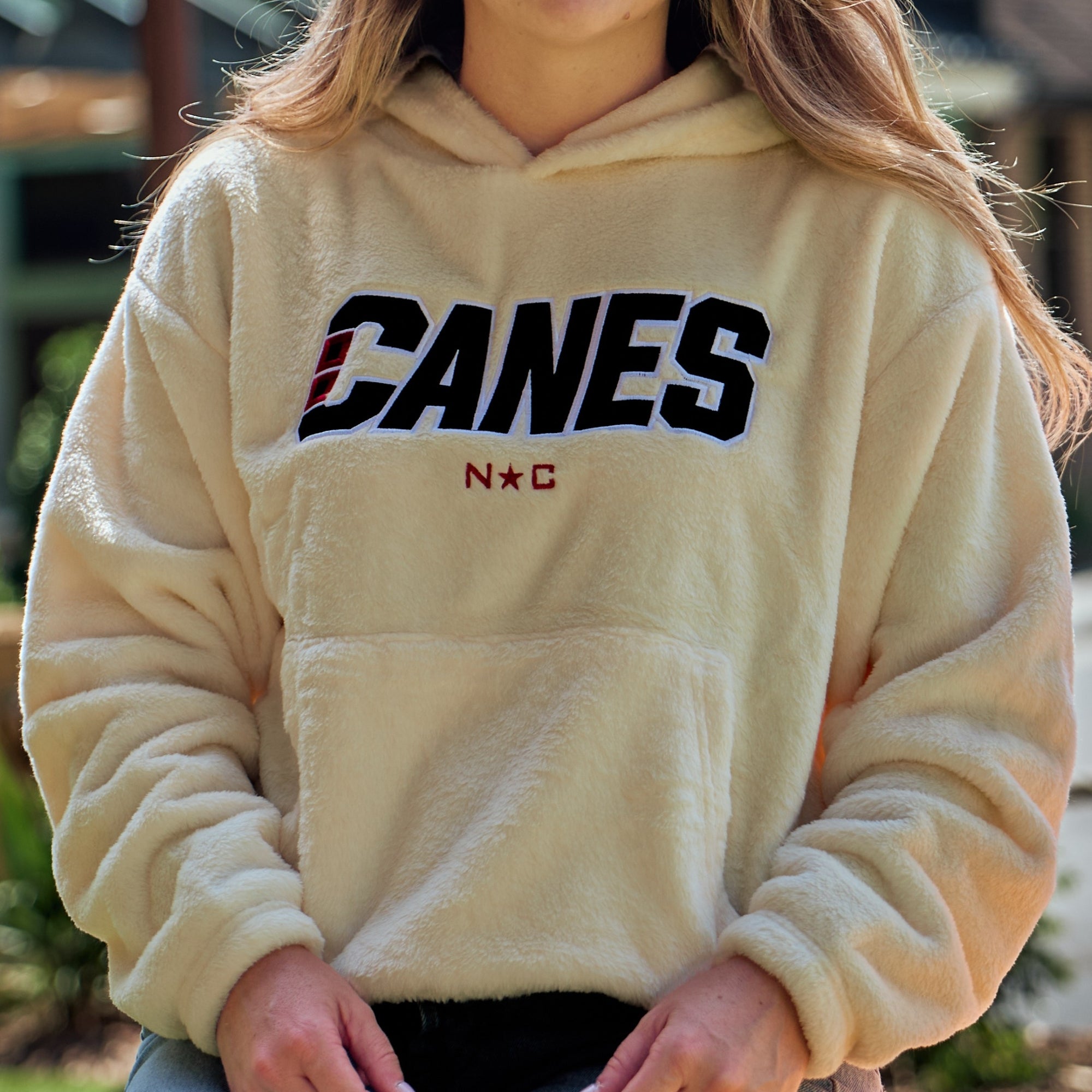 Cream fleece hoodie, "CANES" wordmark/red NC insignia across front