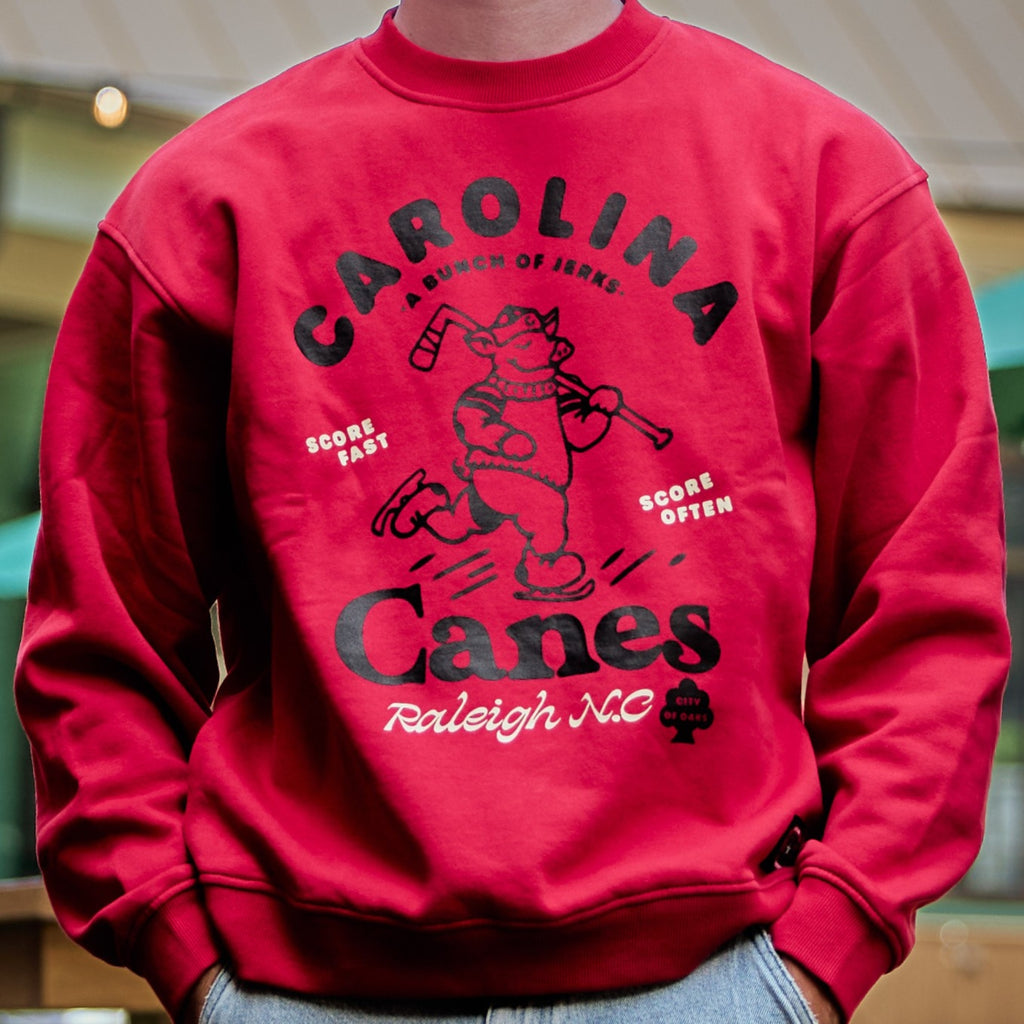 Red crewneck, black/white art on front featuring ice-skating pig, "CAROLINA CANES" with various slogans