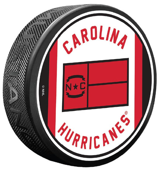 White puck, red/black trim, "CAROLINA HURRICANES" in red arched around Jersey Flag logo