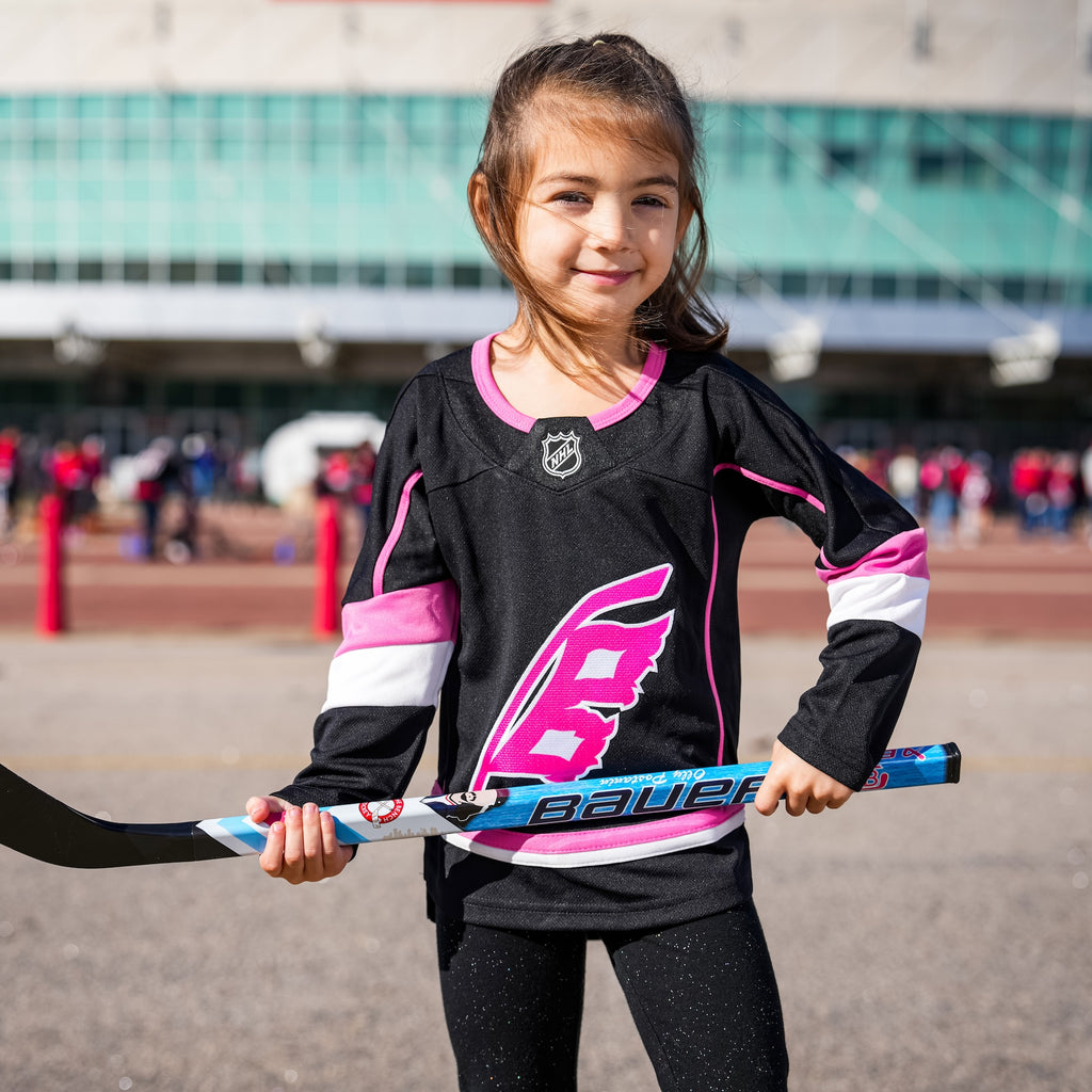 A kid holding a mini hockey stick while wearing the jersey
