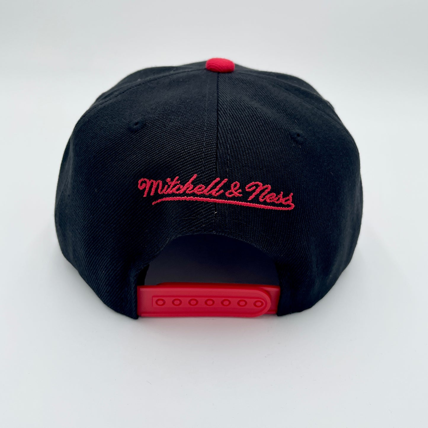 Back: Black hat with red snapback straps, red crown, red Mitchell & Ness wordmark above straps