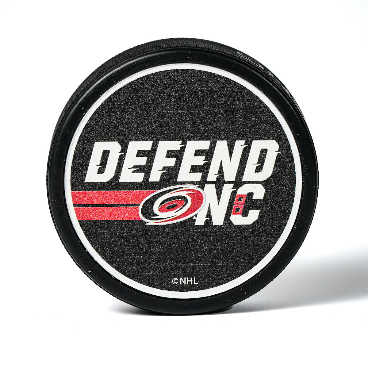 Hockey puck with a "Defend NC" graphic in white with the Hurricanes primary logo on a black top face.