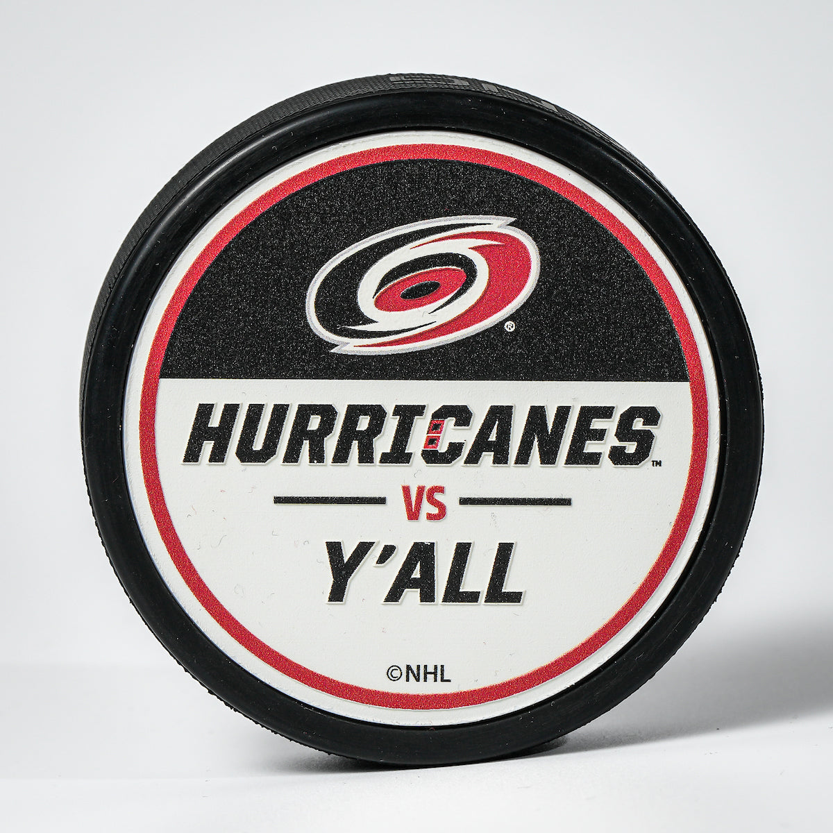 Hockey puck with the Hurricanes primary logo and the phrase "Hurricanes Vs. Y'all" on a black and white top face.