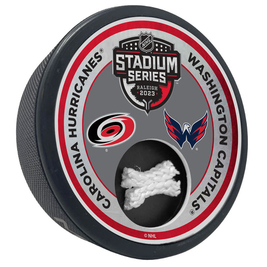 Hockey puck with the Carolina Hurricanes and Washington Capitals logos, along with the 2023 Stadium Series logo and a piece of game-used netting from the Stadium Series on a red and grey top face.